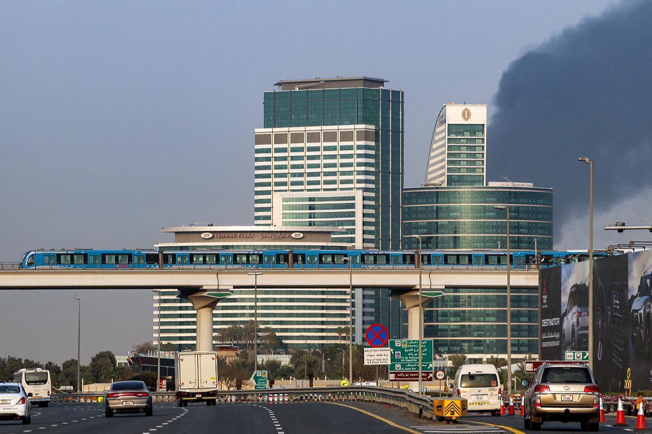 Smoke billows from an ongoing fire near Dubai International Airport as a train of the Dubai Metro moves over vehicles on a highway in Dubai, March 16, 2026. (AFP Photo)