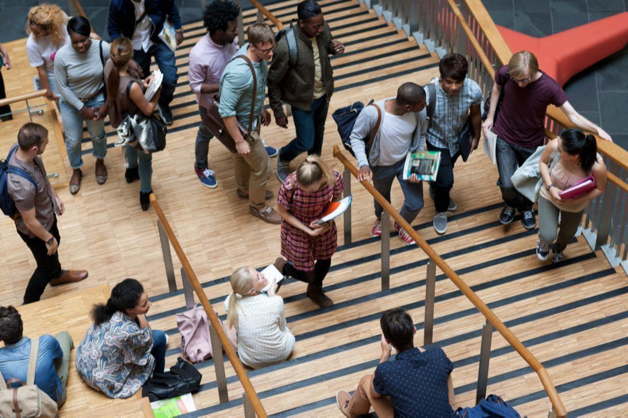 An elevated view shows university students walking up and down a staircase on campus. (Adobe Stock Photo)
