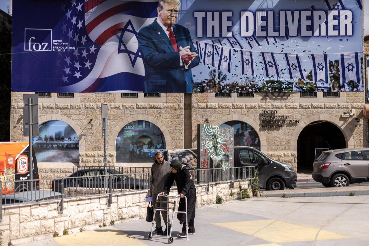 People walk past a banner depicting US President Donald Trump with the slogan "The Deliverer" in Jerusalem on April 22, 2026. (AFP Photo)
