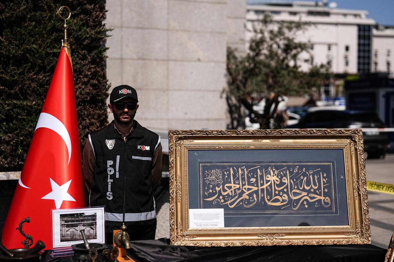 A police officer stands next to seized artifacts, including framed calligraphy and historical objects, following anti-smuggling operations in Istanbul, Türkiye, April 24, 2026. (AA Photo)