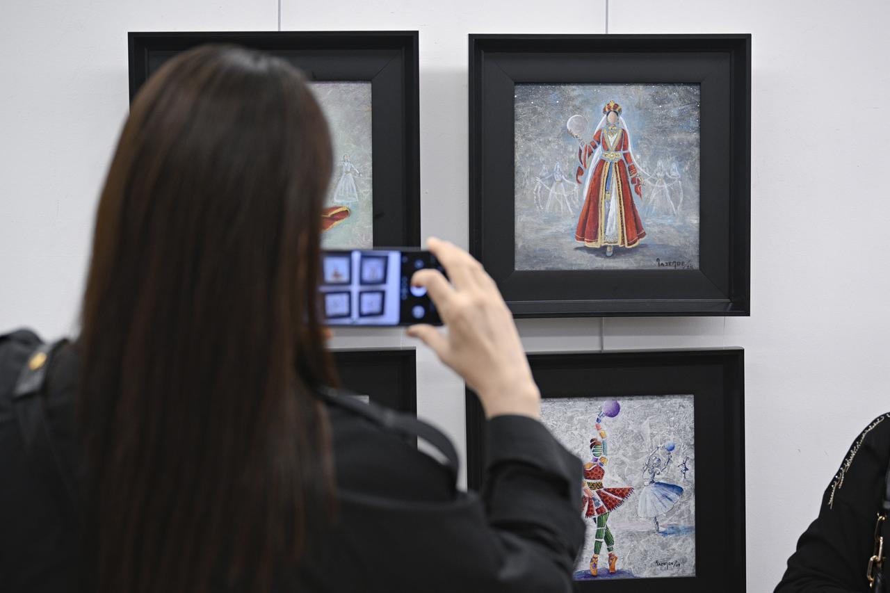 A visitor photographs several paintings displayed at Nazende Yucel’s "Ever-Blooming Women" exhibition, Ankara, Türkiye, April 25, 2026. (AA Photo)