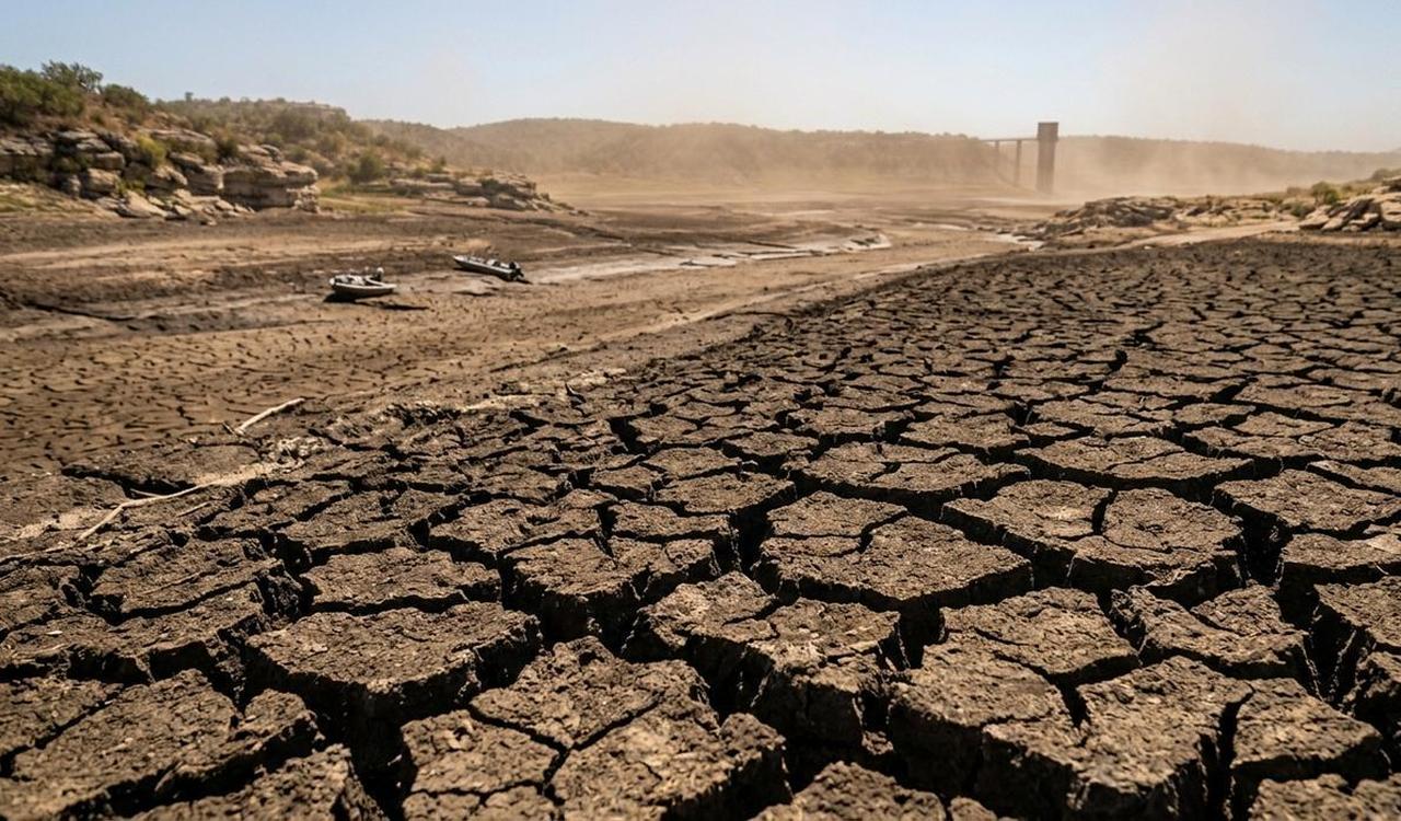 Cracked ground and a dried riverbed are seen in a drought-affected landscape with abandoned boats (Photo generated by Gemini)