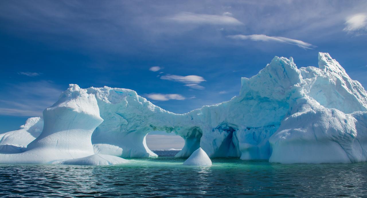 Large iceberg formation with arch-shaped opening floating in open water, Antarctica. (Adobe Stock Photo)