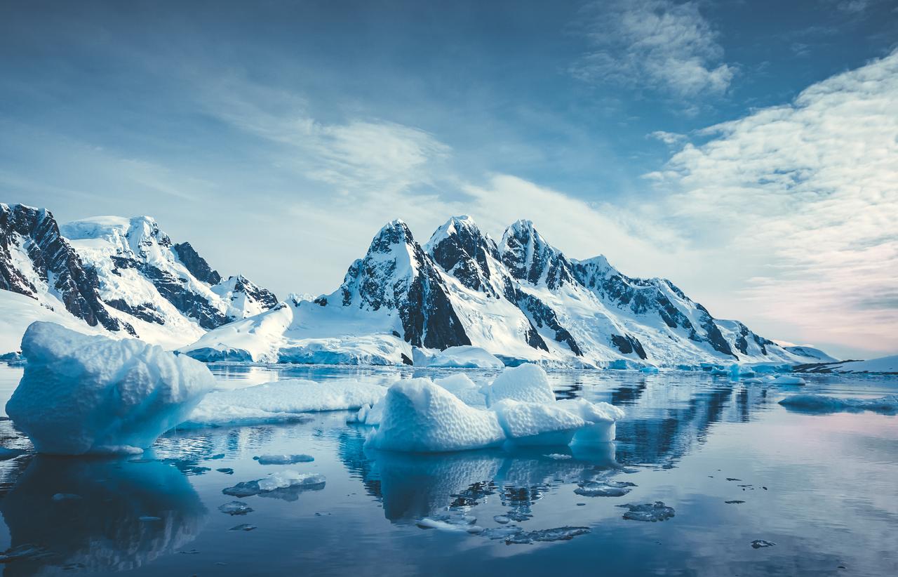Floating ice and snow-covered mountains reflected in clear polar waters under cloudy skies, Southern Ocean, Antarctica. (Adobe Stock Photo)