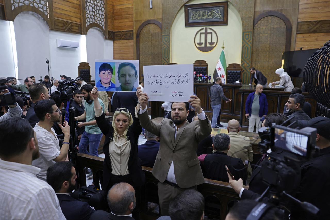 People hold placards at the Palace of Justice ahead of the first trial session, in Damascus on April 26, 2026. (AFP photo)