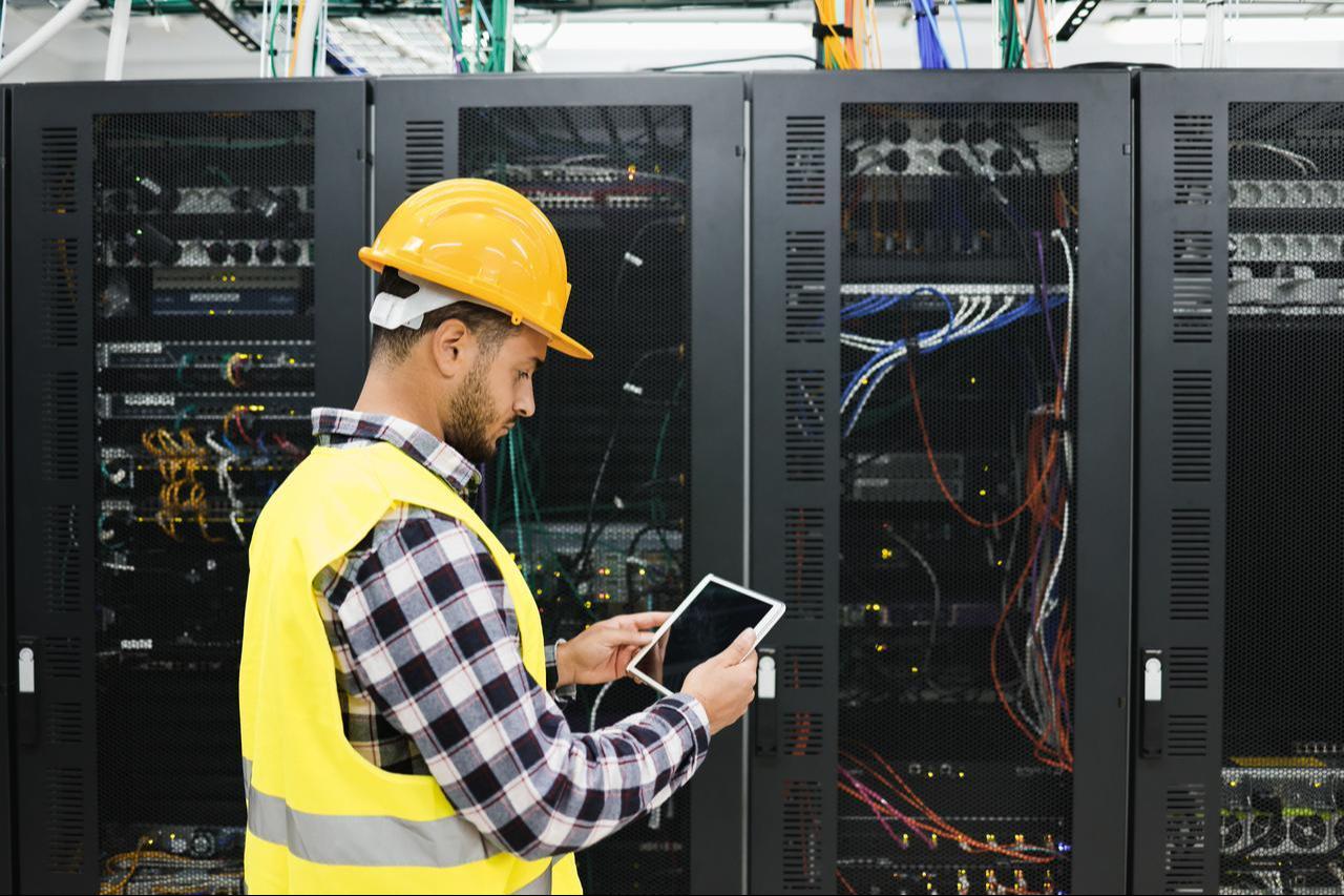 A technician uses a tablet while inspecting server racks at a data center. (Adobe Stock Photo)