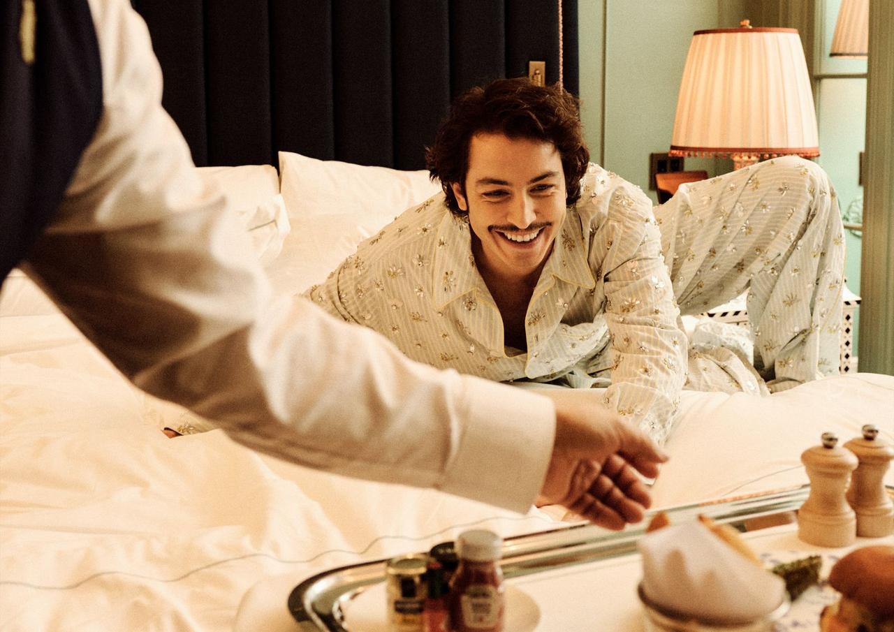 Boran Kuzum smiles while lounging on a bed during a styled hotel shoot scene, New York, United States, April 29, 2026. (Courtesy of BKM)