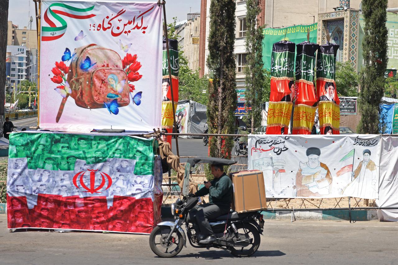 A motorist rides past a banner with illustrations of Iran's slain supreme leader Ali Khamenei and an Iranian flag installed along the roadside in Tehran, Iran, April 29, 2026. (AFP Photo)