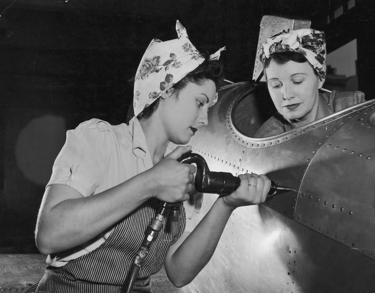 Female factory workers wearing red lipstick drive rivets into an aircraft fuselage in Long Beach, California, circa 1943. (Courtesy of Medium)