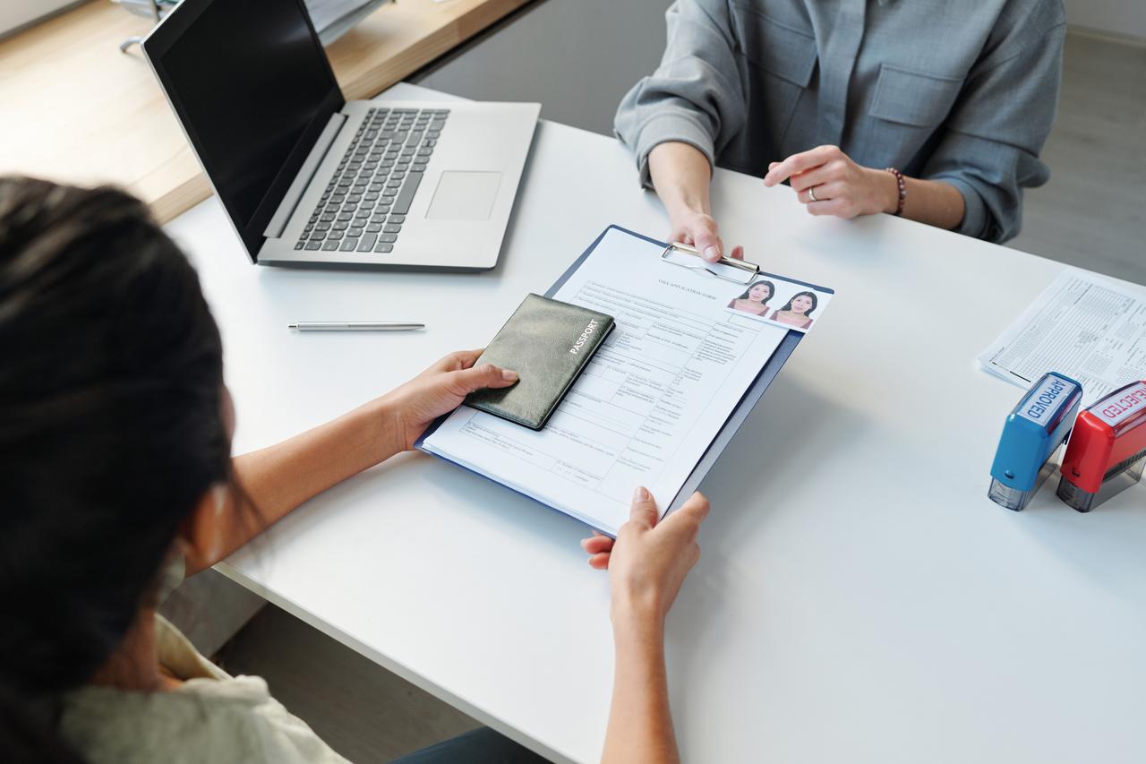 A visa applicant submits a passport and application form to a consular officer at an embassy office in an undated stock photo. (Adobe Stock Photo)