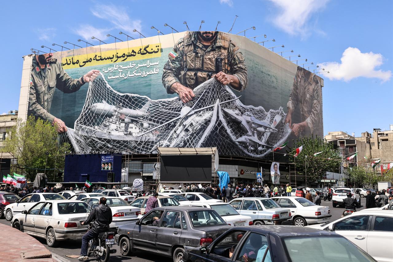 Vehicles drive past a large billboard reading "The Strait of Hormuz remains closed" as people gather in Tehran's Revolution Square, April 8, 2026. (AFP Photo)