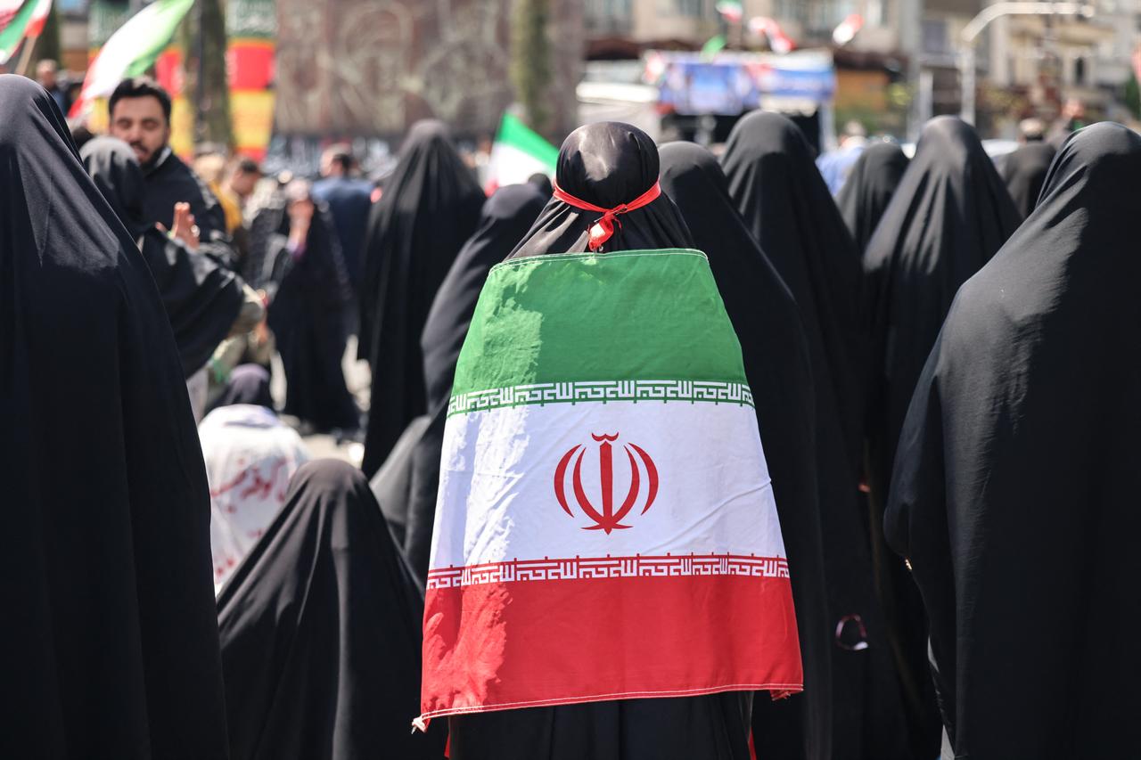 An Iranian woman wrapped in the national flag performs noon prayers as people gather in Tehran's Revolution Square after the United States and Iran agreed to a two-week ceasefire, April 8, 2026. (AFP Photo)