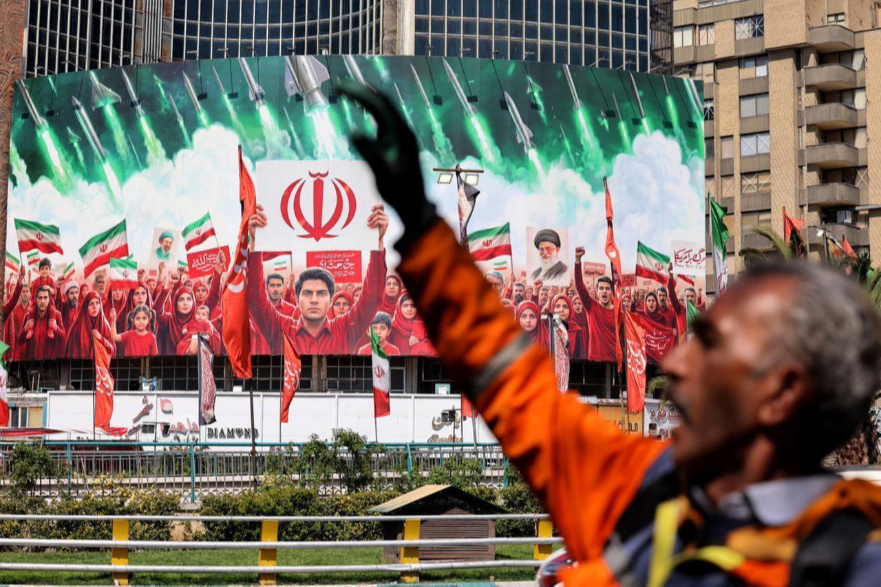 A municipal worker gestures near a large political banner, depicting missiles being fired behind Iranian demonstrators, at Valiasr Square in Tehran, April 6, 2026. (AFP Photo)