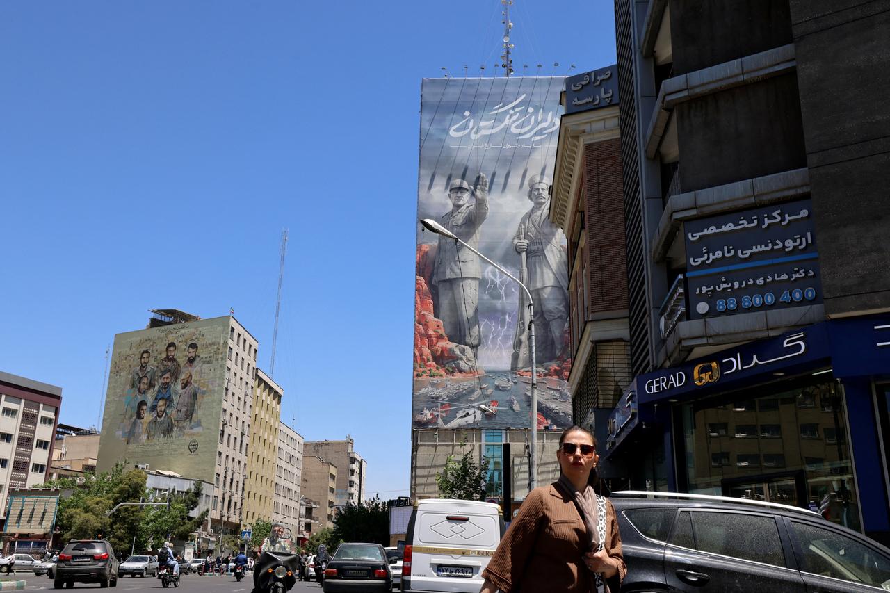 A woman walks along a busy street near a huge mural painted on the side of a building referring to the 'Strait of Hormuz' (R), in the capital Tehran on May 9, 2026. (AFP Photo)