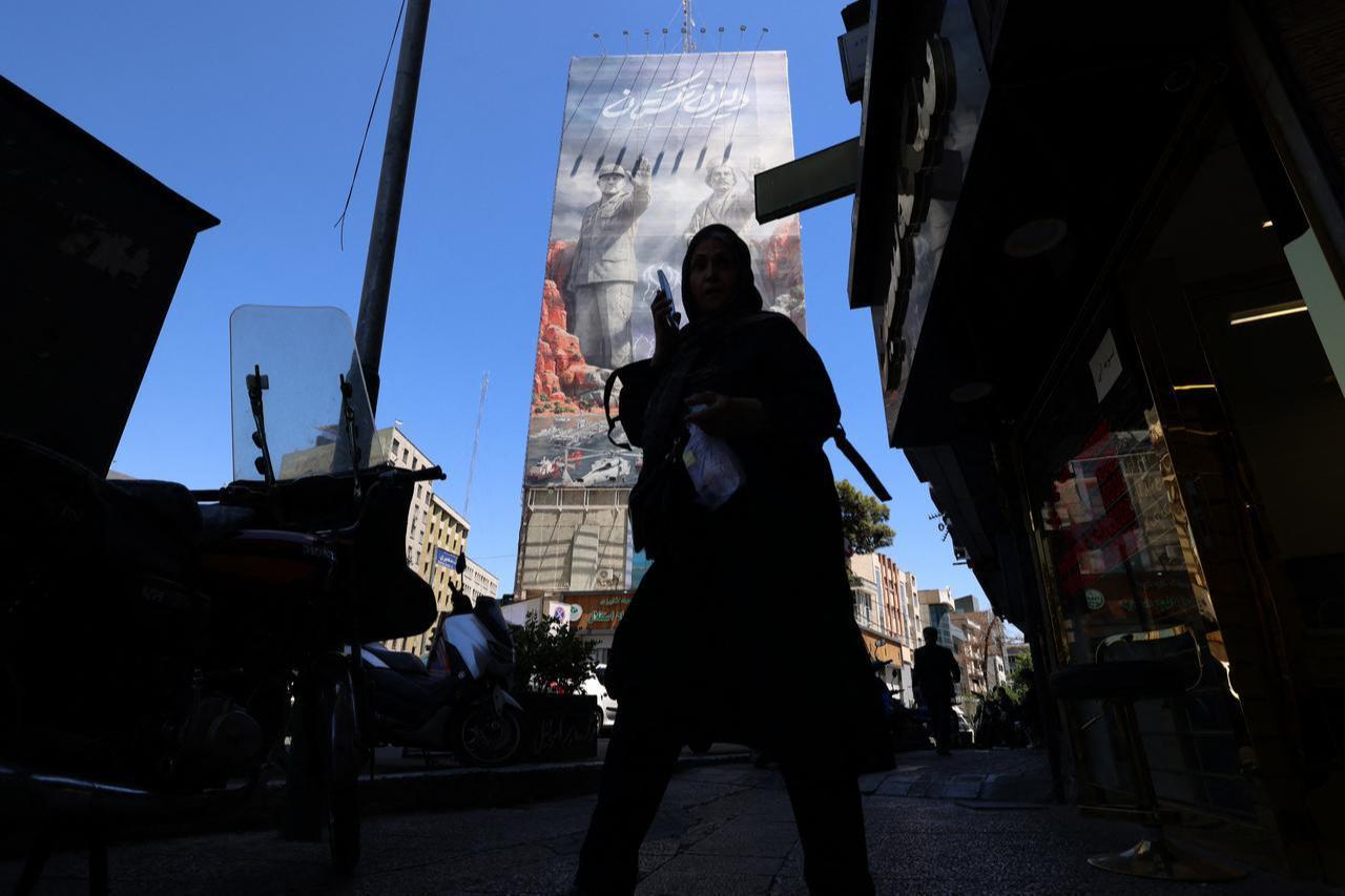 A woman walks along a busy street near a huge mural painted on the side of a building referring to the 'Strait of Hormuz', in the capital Tehran, May 9, 2026. (AFP Photo)