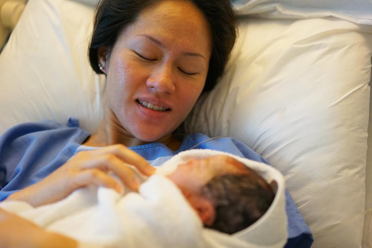 A woman holds her newborn baby in a hospital bed. (Adobe Stock Photo)