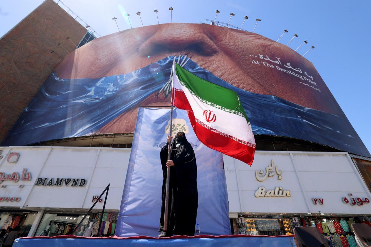 A woman holds the Iranian flag as she stands in front of an anti-US billboard referring to President Donald Trump and the Strait of Hormuz, at the Valiasr Square in Tehran on May 10, 2026. (AFP Photo)