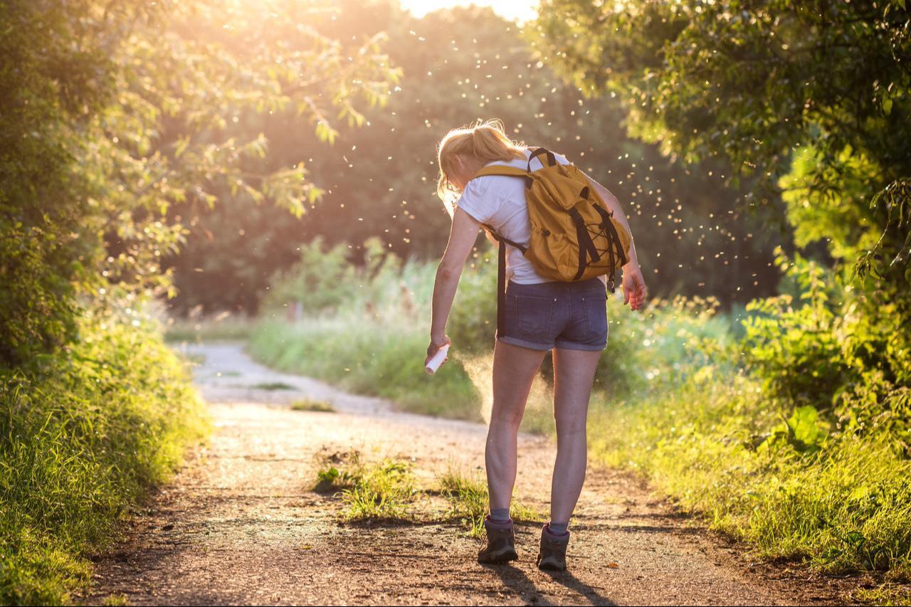 A woman sprays insect repellent while walking along a wooded trail (Adobe Stock Photo)