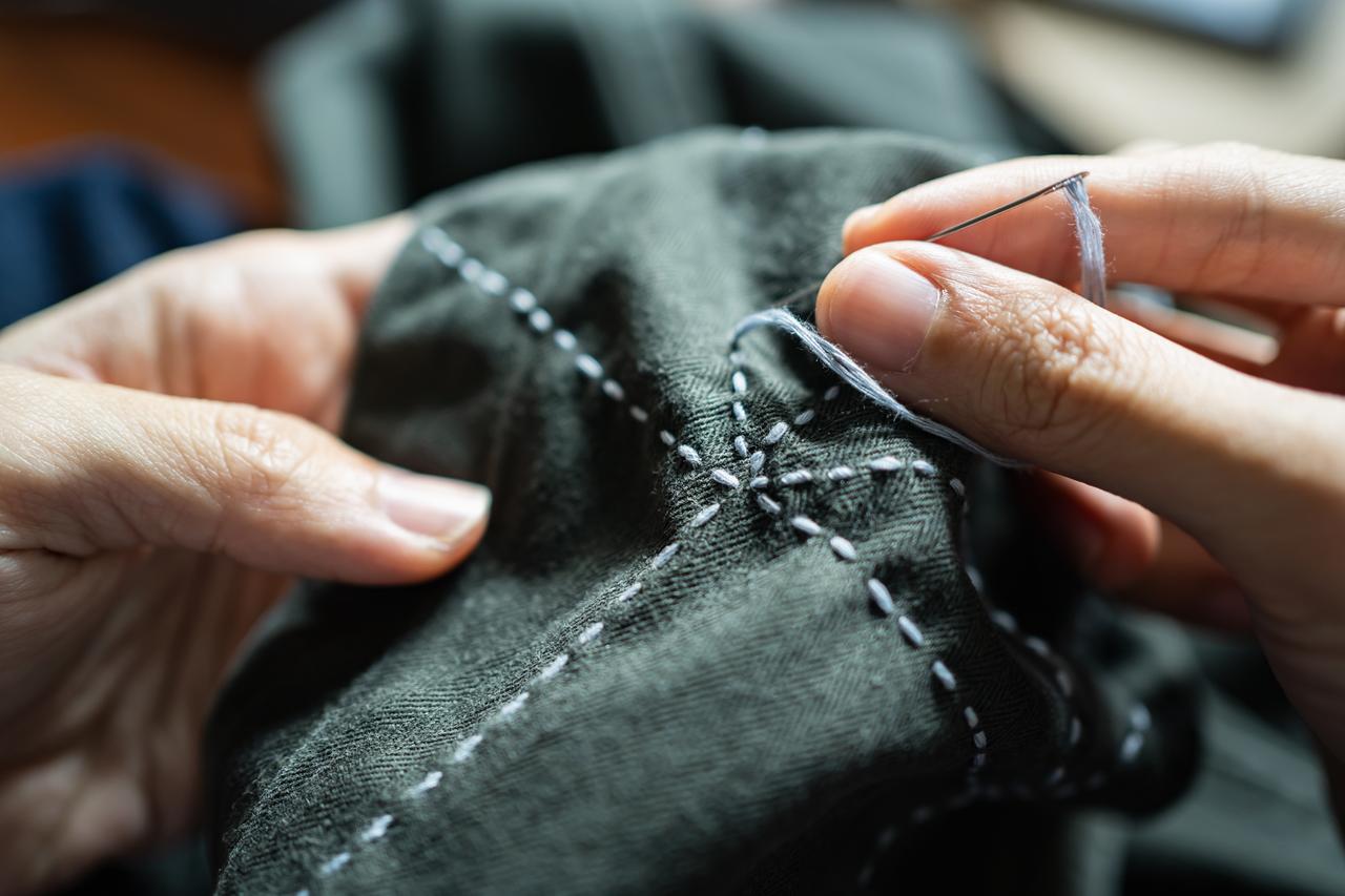 Hands sew decorative stitching onto dark fabric in a close-up (Adobe Stock Photo)