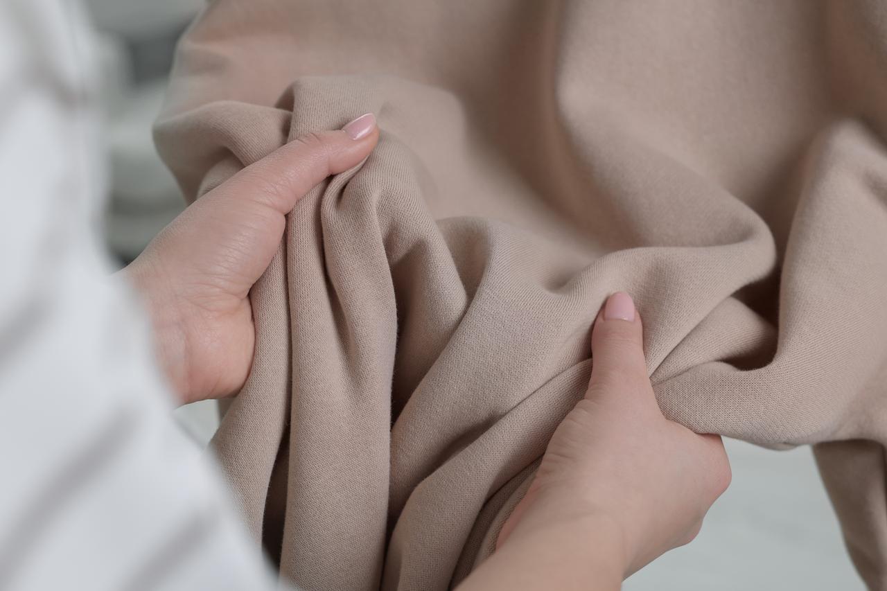Hands hold and examine a piece of soft beige fabric (Adobe Stock Photo)