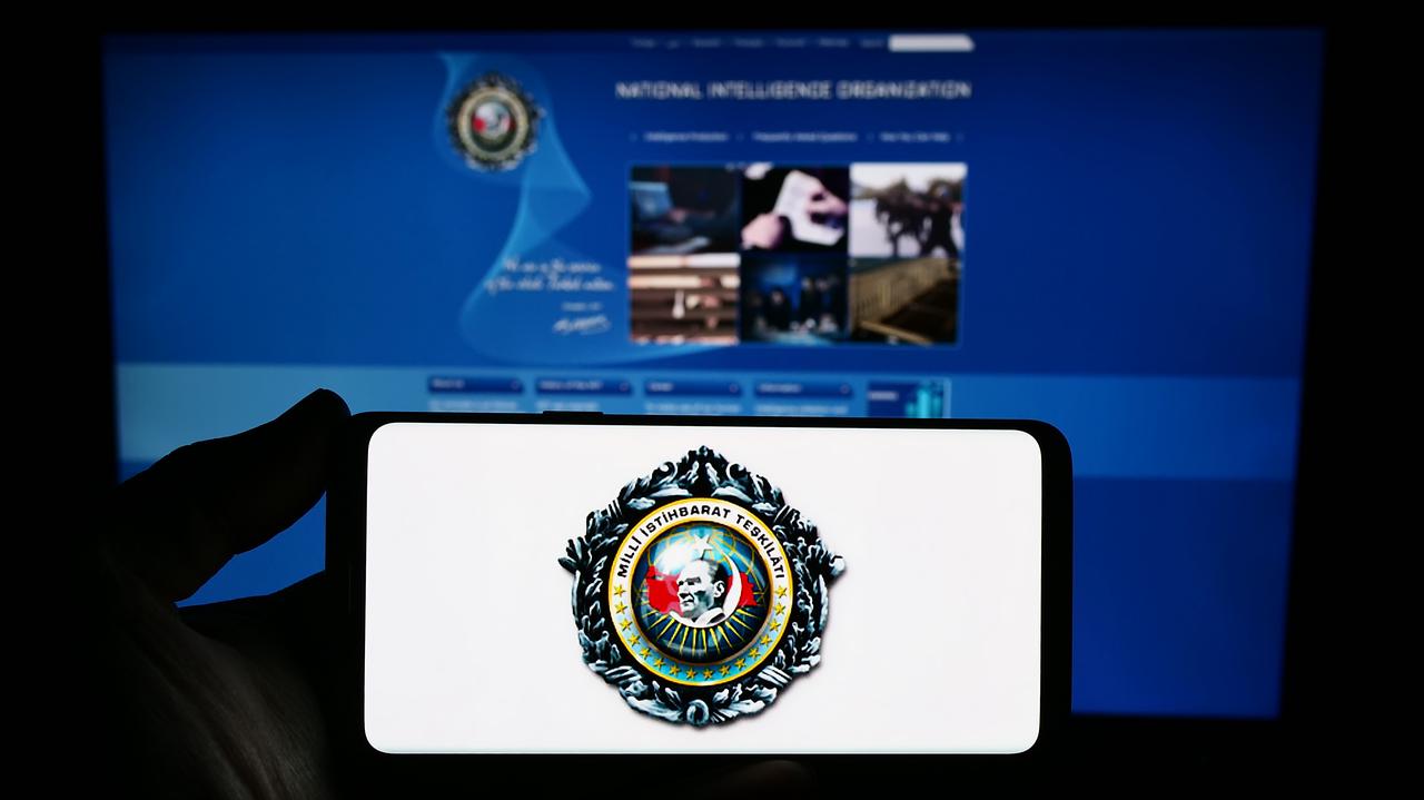 Person holding smartphone with logo of Turkish intelligence agency in front of its website, accessed on May 16, 2026. (Adobe Stock Photo)
