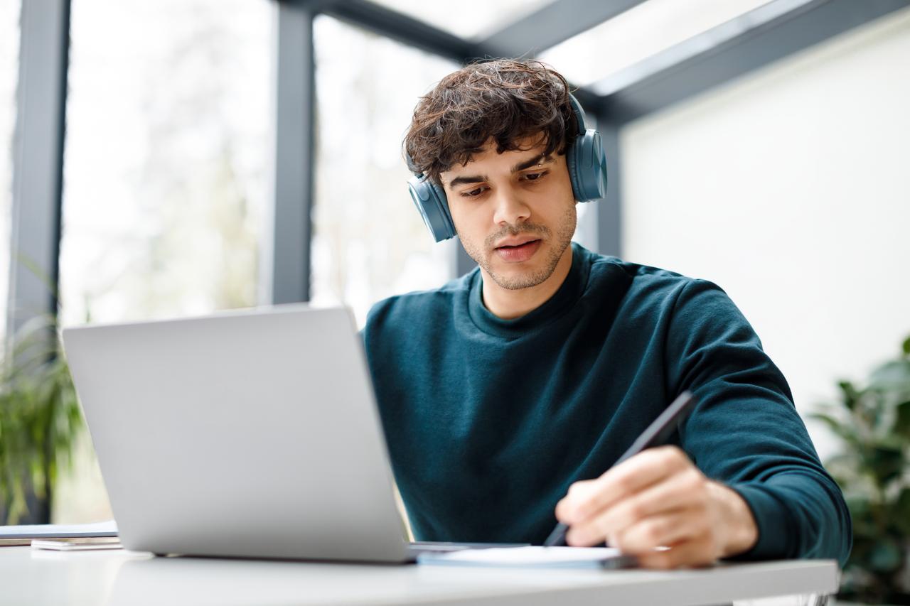 A student studies on a laptop while wearing headphones in a home or remote learning environment. (Adobe Stock Photo)