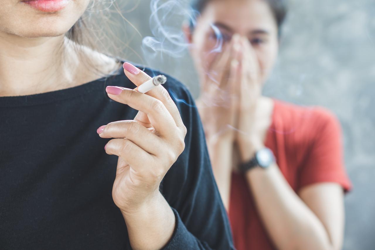 A woman smokes a cigarette while another person reacts to the smoke,. (Adobe Stock Photo)