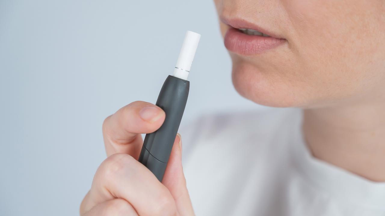 A close-up of a person holding a sleek black heated tobacco device near their lips, highlighting modern alternative smoking technology and minimalist lifestyle habits. (Adobe Stock Photo)