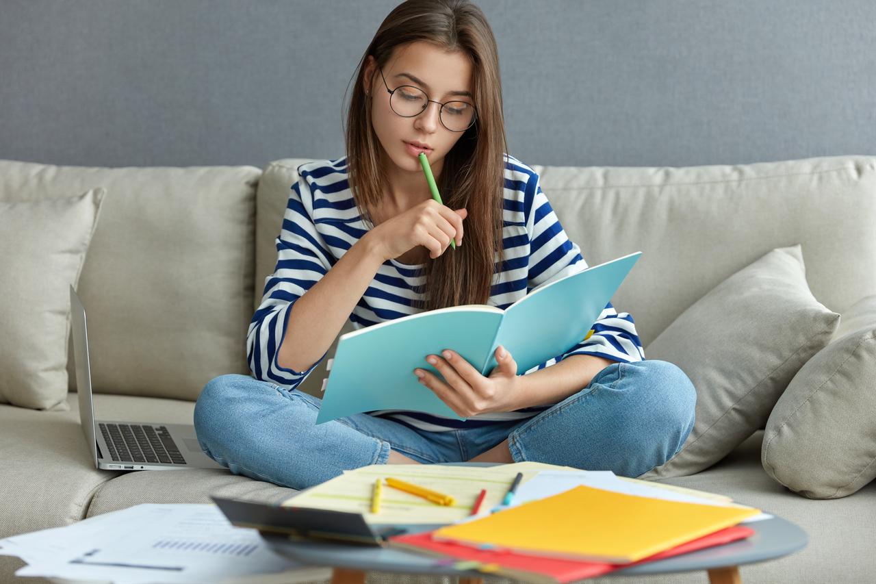 A woman studies with a notebook and laptop at home (Adobe Stock Photo)