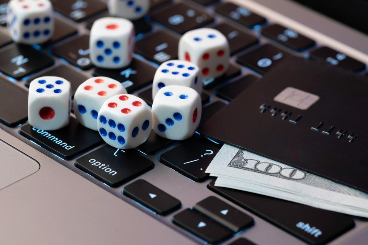 Close-up of dice placed on a computer keyboard next to a credit card and cash, symbolizing online gambling and digital betting transactions. (Adobe Stock Photo)