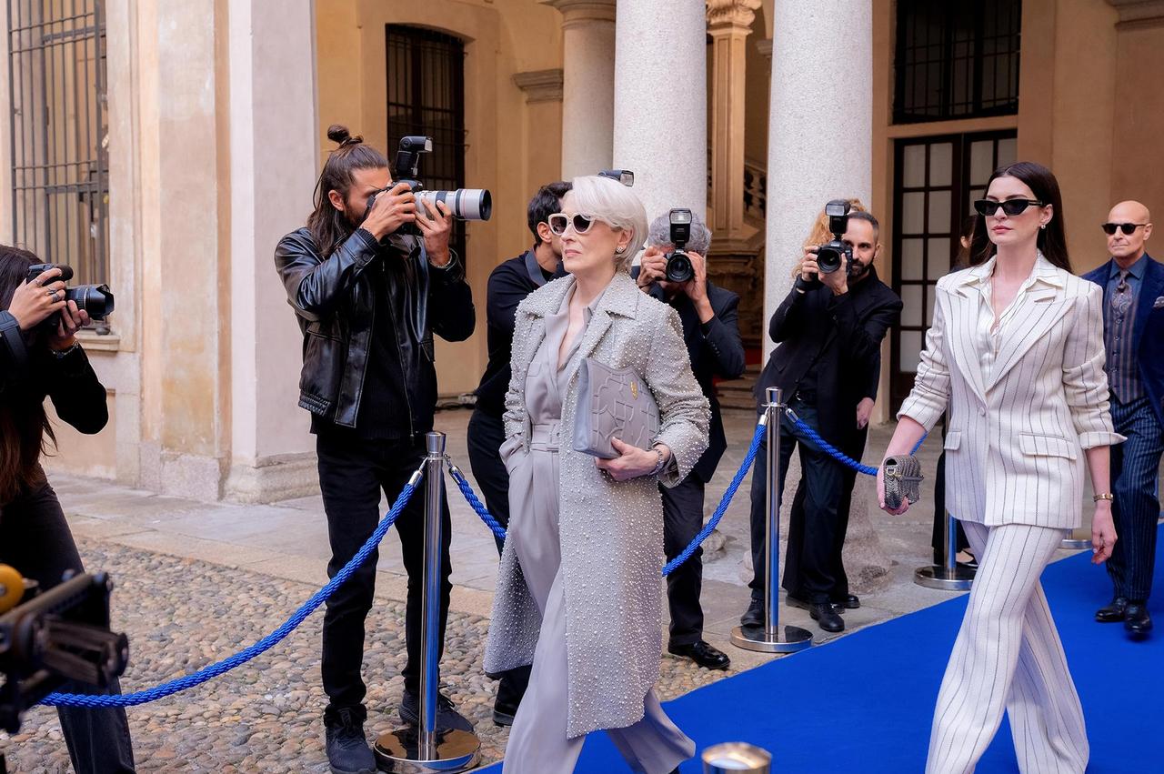 Miranda Priestly and Andy Sachs walk past photographers on a blue carpet in a scene from "The Devil Wears Prada 2," accessed on May 2, 2026. (Courtesy of IMDb)