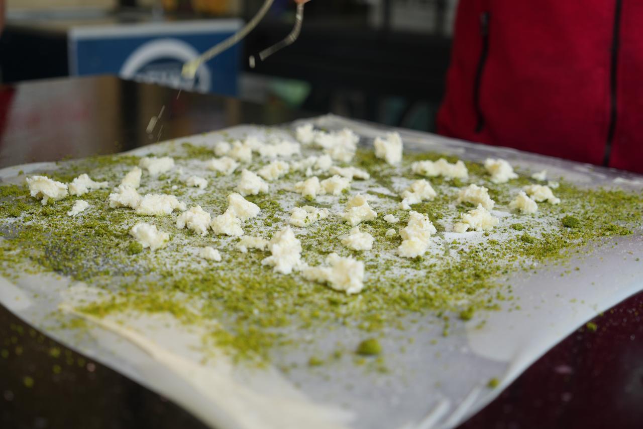 Fresh clotted cream (kaymak) distributed over Antep pistachios and dough during the katmer preparation process. (IHA Photo)