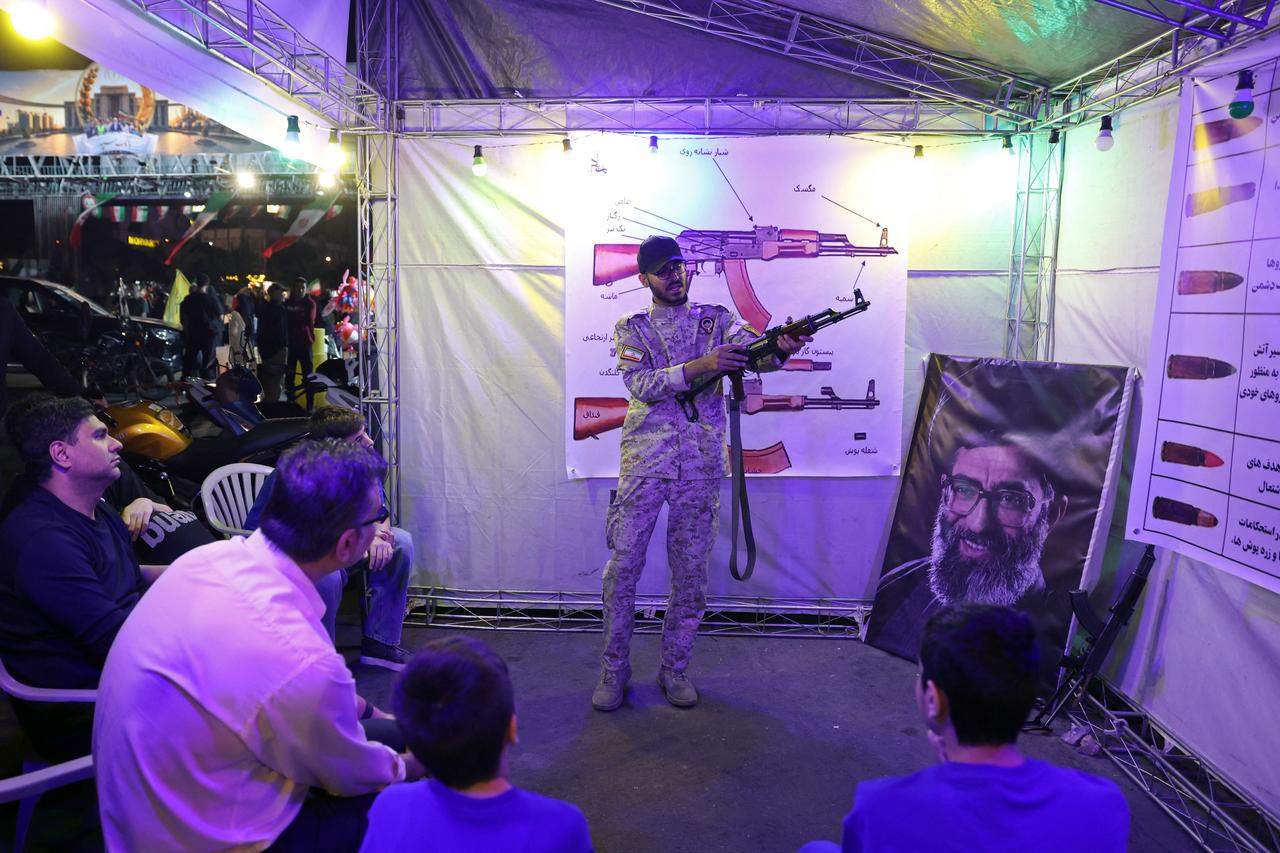An Iranian military personnel (C) educates people about how to use a gun at a booth in Hafte Tir Square, in Tehran on May 17, 2026. (AFP Photo)