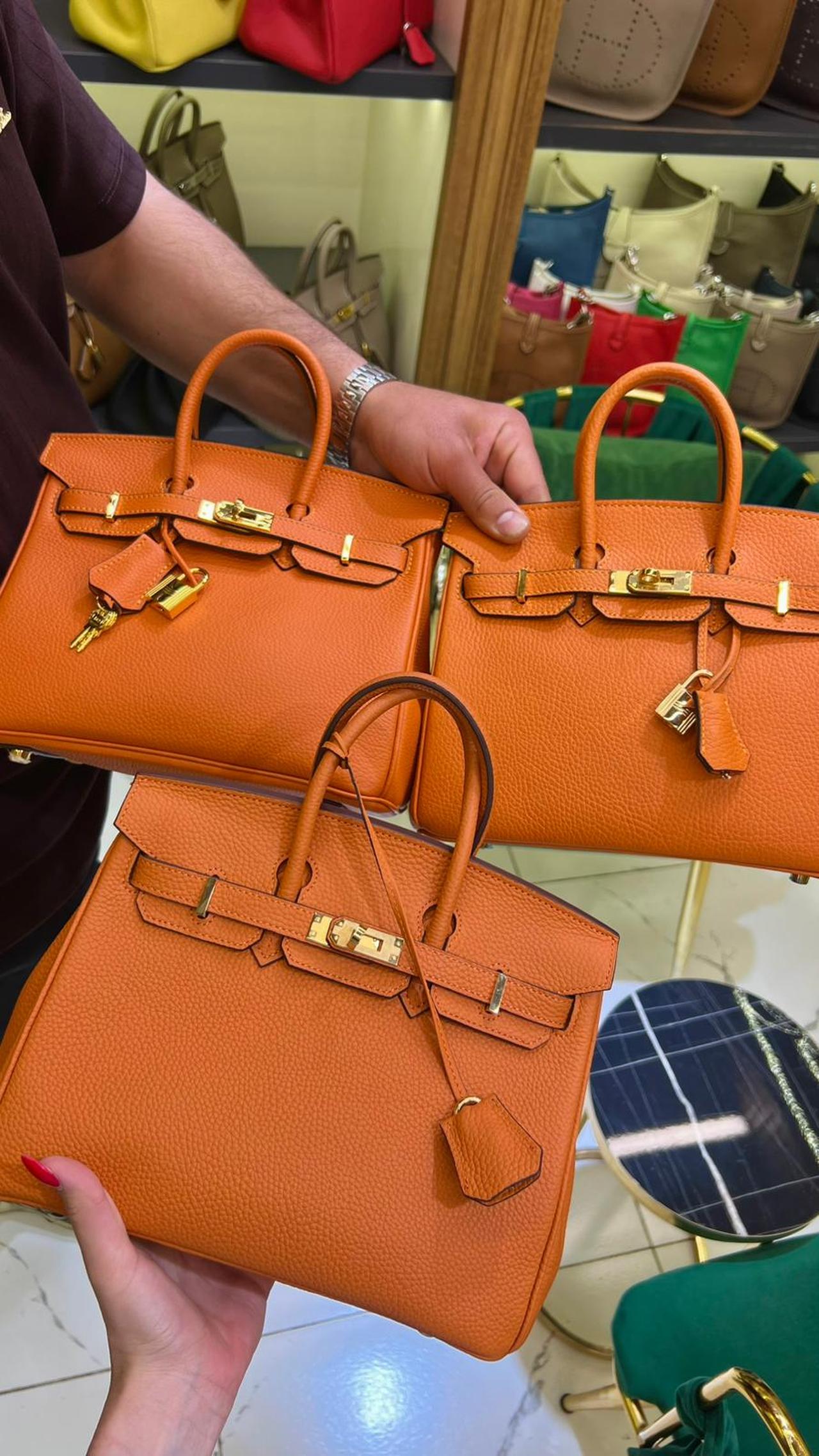 The seller in Istanbul’s replica market places three nearly identical orange handbags side by side to explain how quality alters price, texture, and perceived authenticity. (Photo by Türkiye Today)