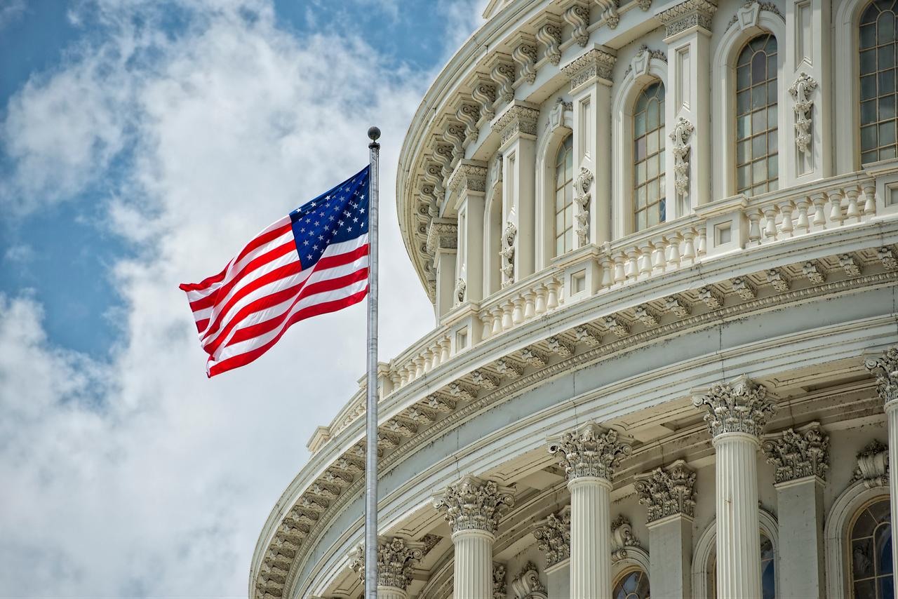 A U.S. flag waves beside the U.S. Capitol building in Washington, D.C., United States. (Adobe Stock Photo)