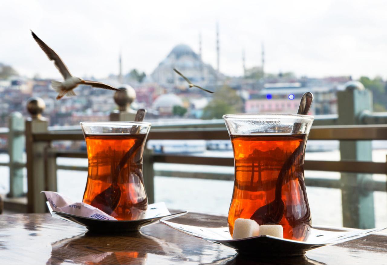 A steaming Turkish tea cup with the iconic backdrop of Istanbul's bustling port, where tradition meets the sea. (Adobe Stock Photo)