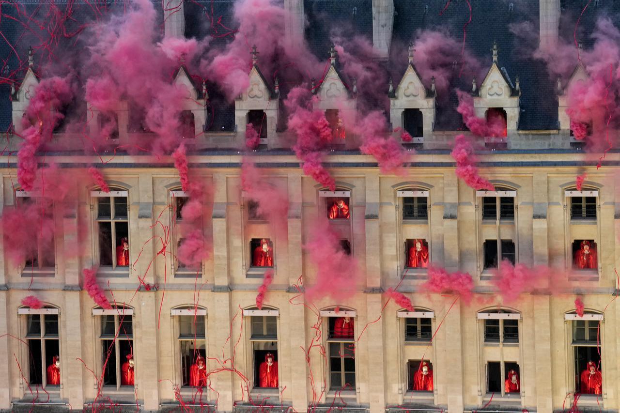 This image depicts a performance from the Paris 2024 Olympic Games Opening Ceremony at the Conciergerie, featuring headless Marie-Antoinette figures singing from windows amidst red smoke and streamers.