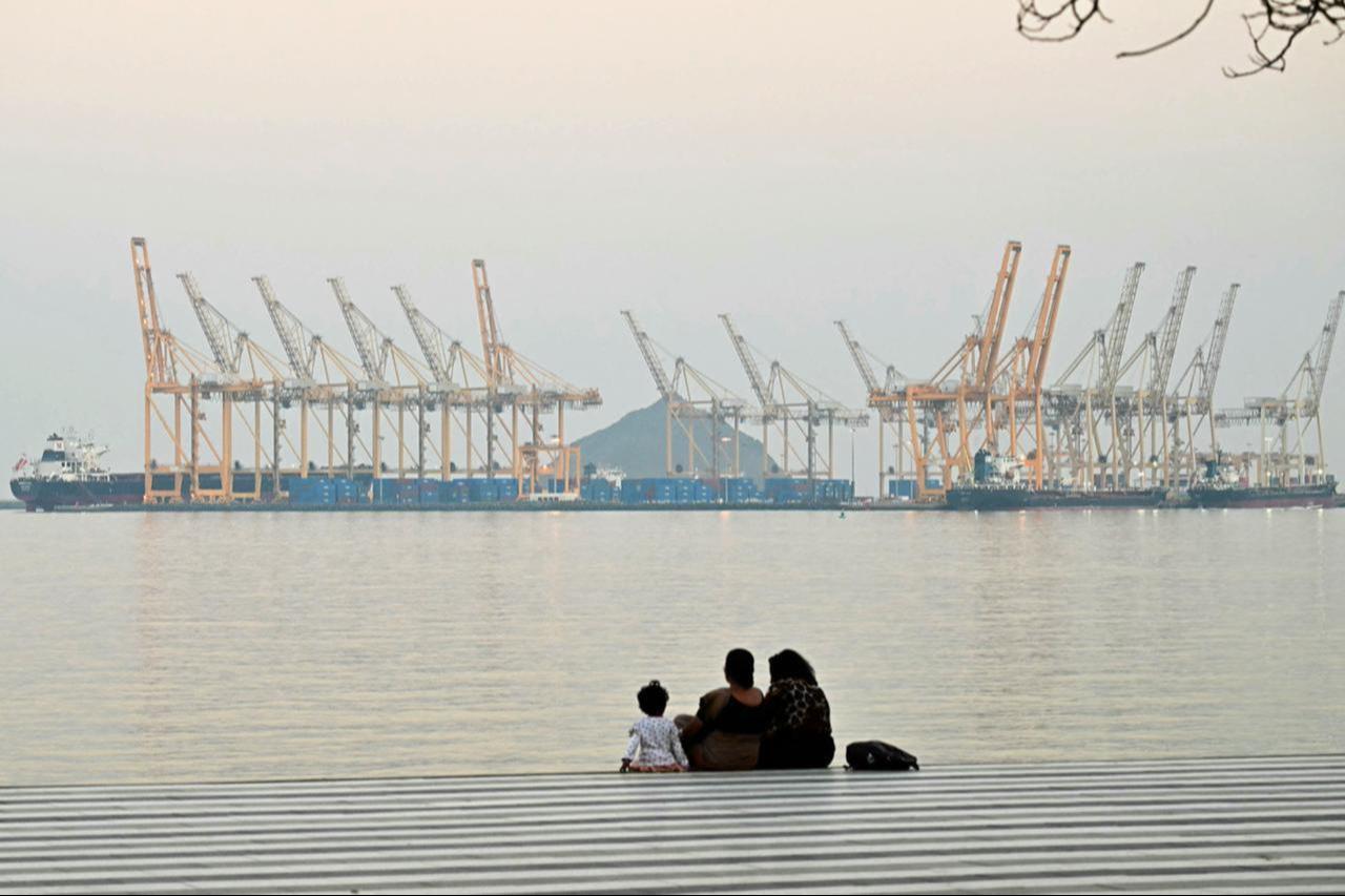 A family sits against the backdrop of a dockyard off coast city of Fujairah, in the Strait of Hormuz in the northern Emirate, February 25, 2026. (AFP Photo)