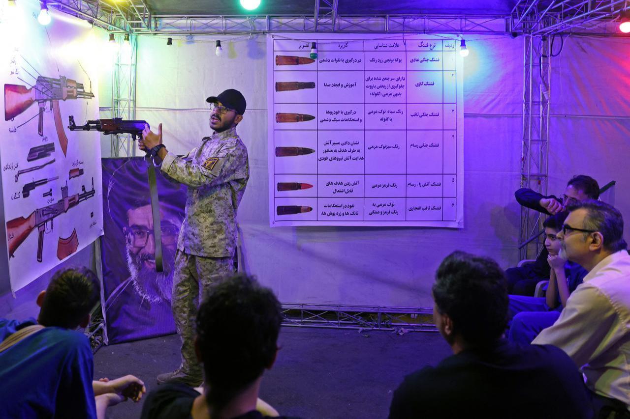An Iranian military personnel (L) educates people about how to use a gun at a booth in Hafte Tir Square, in Tehran on May 17, 2026. (AFP Photo)