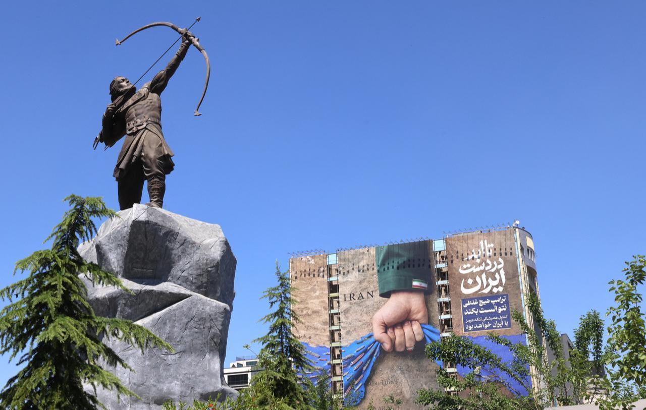 A billboard on the facade of a building depicting the Strait of Hormuz with a caption in Persian reading "Forever in Iran’s Hand", is the backdrop to a modern sculpture of Arash the Archer, in Vanak Square in Tehran, May 25, 2026. (AFP Photo)