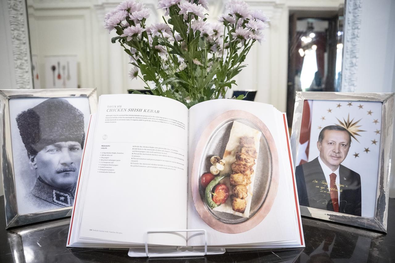 A cookbook featuring Turkish dishes is displayed between portraits of Mustafa Kemal Ataturk and President Recep Tayyip Erdogan during Turkish Cuisine Week, May 21, 2026. (AA Photo)