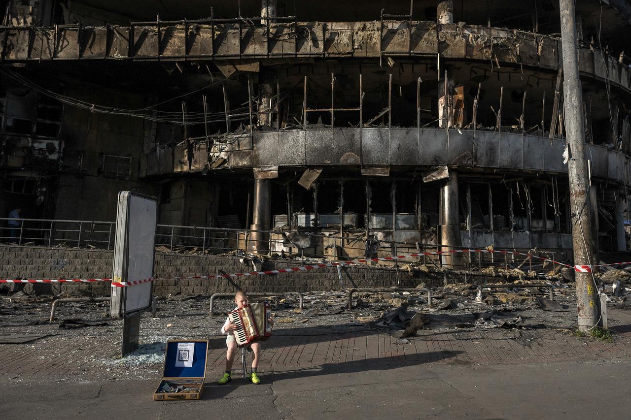 A boy plays the accordion in front of a shopping center damaged by Russian strikes in Kyiv on May 25, 2026. (AFP Photo)