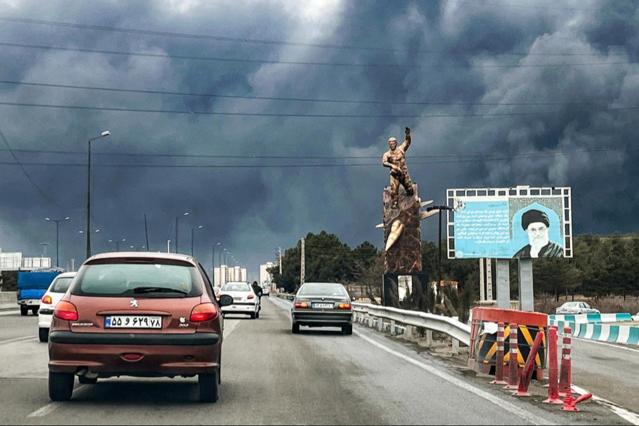 Vehicles move along a highway past a war memorial statue and a billboard depicting Iran's late supreme leader Ali Khamenei who was killed in an air strike, with plumes of black smoke billowing, in Tehran March 8, 2026. (AFP Photo)