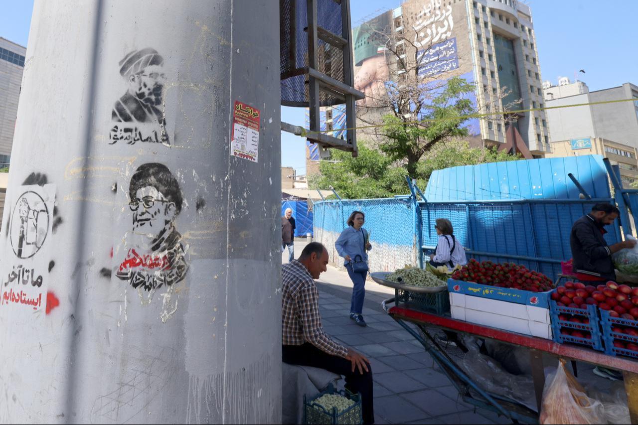 Stencil images of new Iranian leader Mojtaba Khamenei (top) and slain supreme leader Ali Khamenei are sprayed on a lamp post near a fruit vendor on the side of the street in Tehran on May 25, 2026. (AFP Photo)
