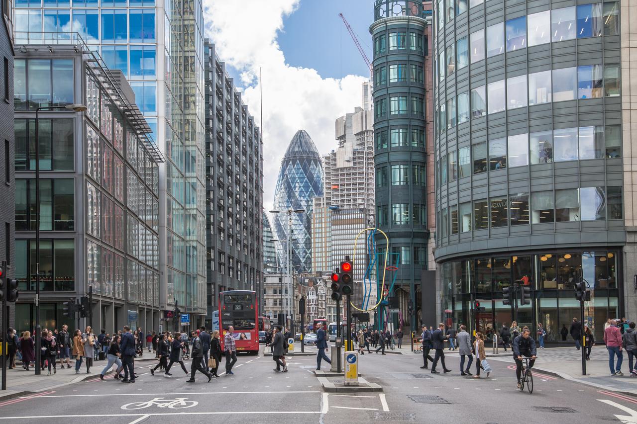 Pedestrians cross a busy street in London’s financial district, with the Gherkin skyscraper visible in the background in London, United Kingdom. (Adobe Stock Photo)