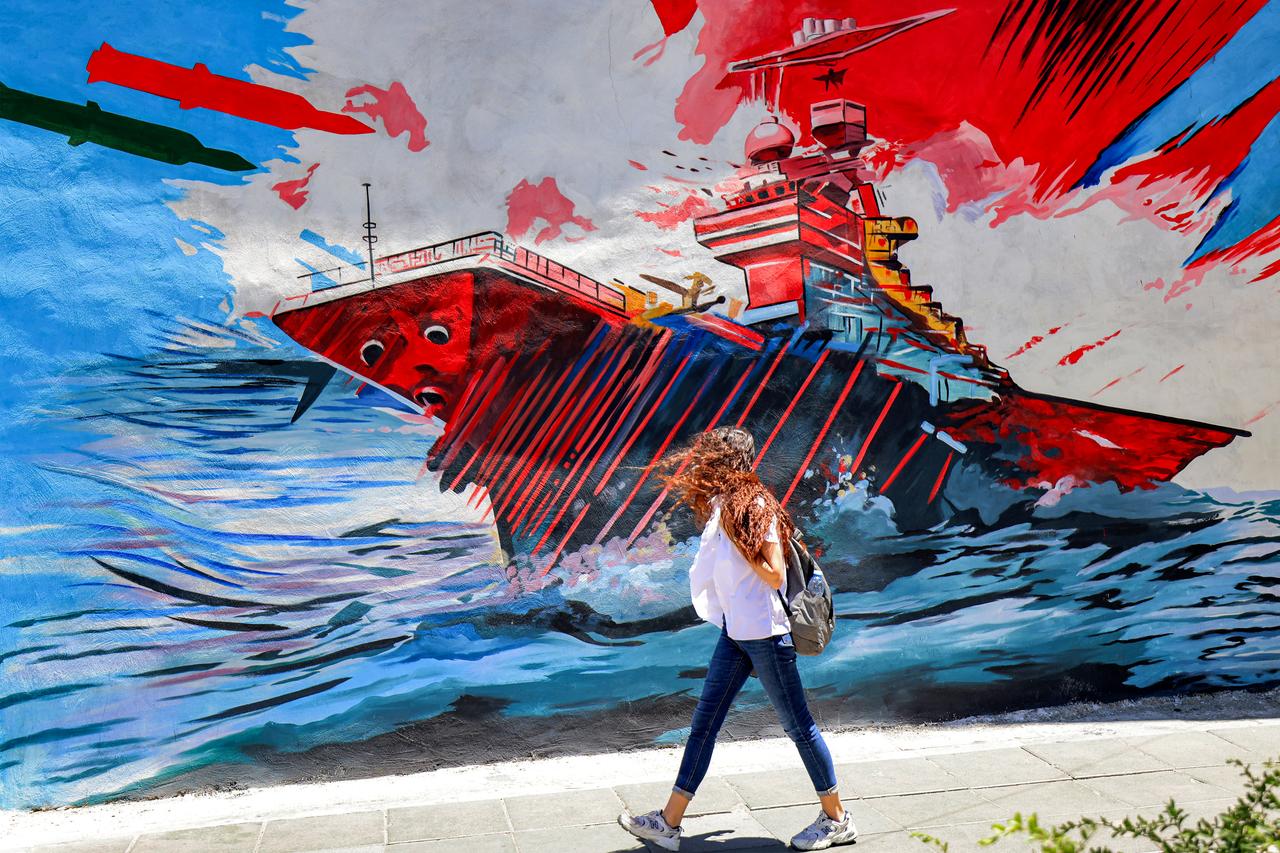 A woman walks past an anti-US and anti-Israel mural depicting missiles hitting an aircraft carrier in Tehran on May 26, 2026. (AFP Photo)