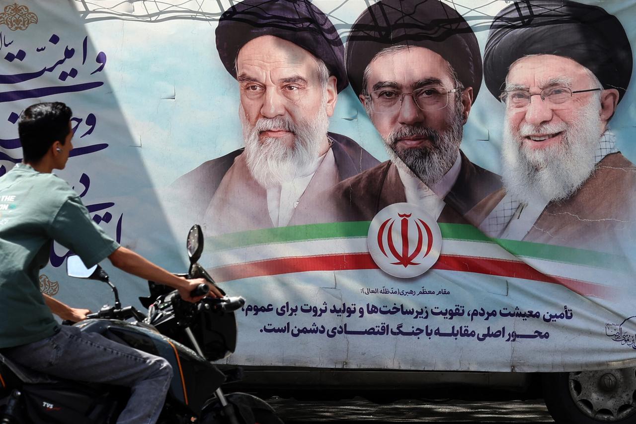 An Iranian man rides his motorbike past a billboard bearing the images of the late founder of the Islamic Revolution Supreme Leader Ruhollah Khomeini (L), the late Iranian supreme leader Ali Khamenei (R), and his son the current supreme leader Mojtaba Khamenei (C), erected along a street in Tehran on May 28, 2026. (AFP Photo)