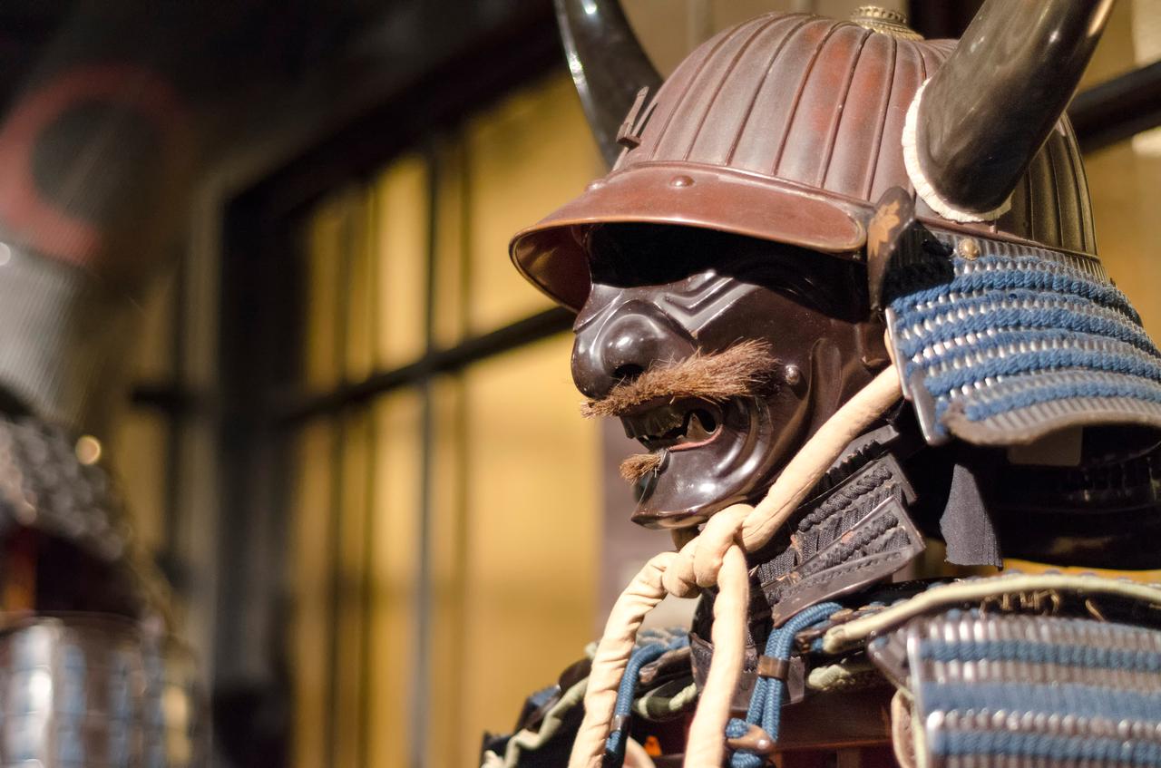 A traditional Japanese samurai armor with a horned helmet and face mask is displayed indoors (Adobe Stock Photo)