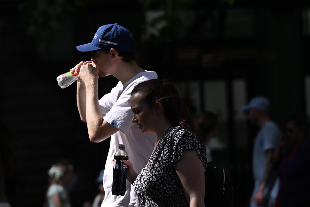People drink cold beverages to cool off as they walk down a street in London, UK, May 23, 2026. (AA Photo)