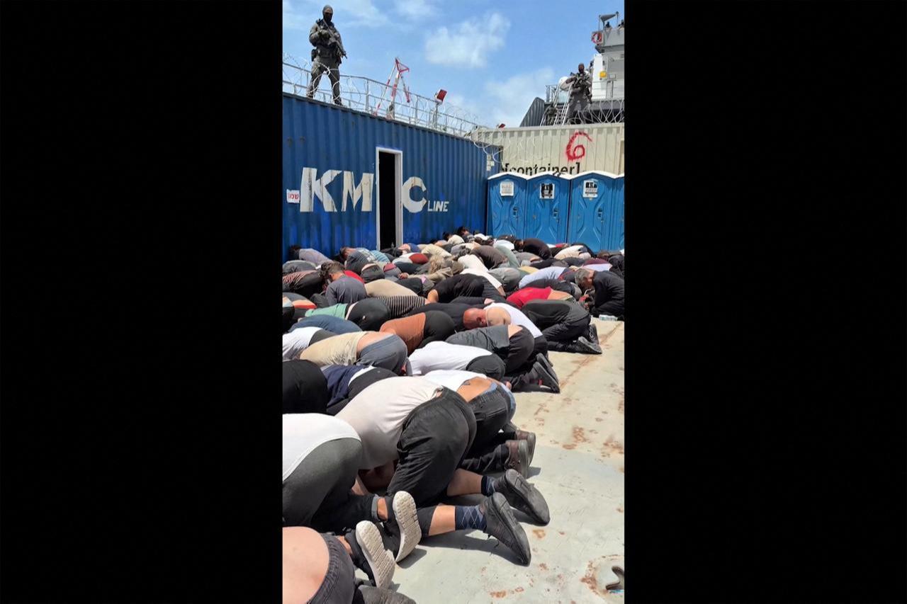 This screen grab, taken from footage released on May 20, 2026, shows dozens of detained activists from the Gaza-bound aid flotilla kneeling with their hands tied behind their backs and their foreheads on the ground. (Photo via X/@itamarbengvir/AFP)